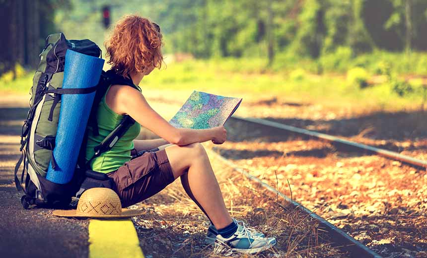 Backpacker sat beside train track reading a map